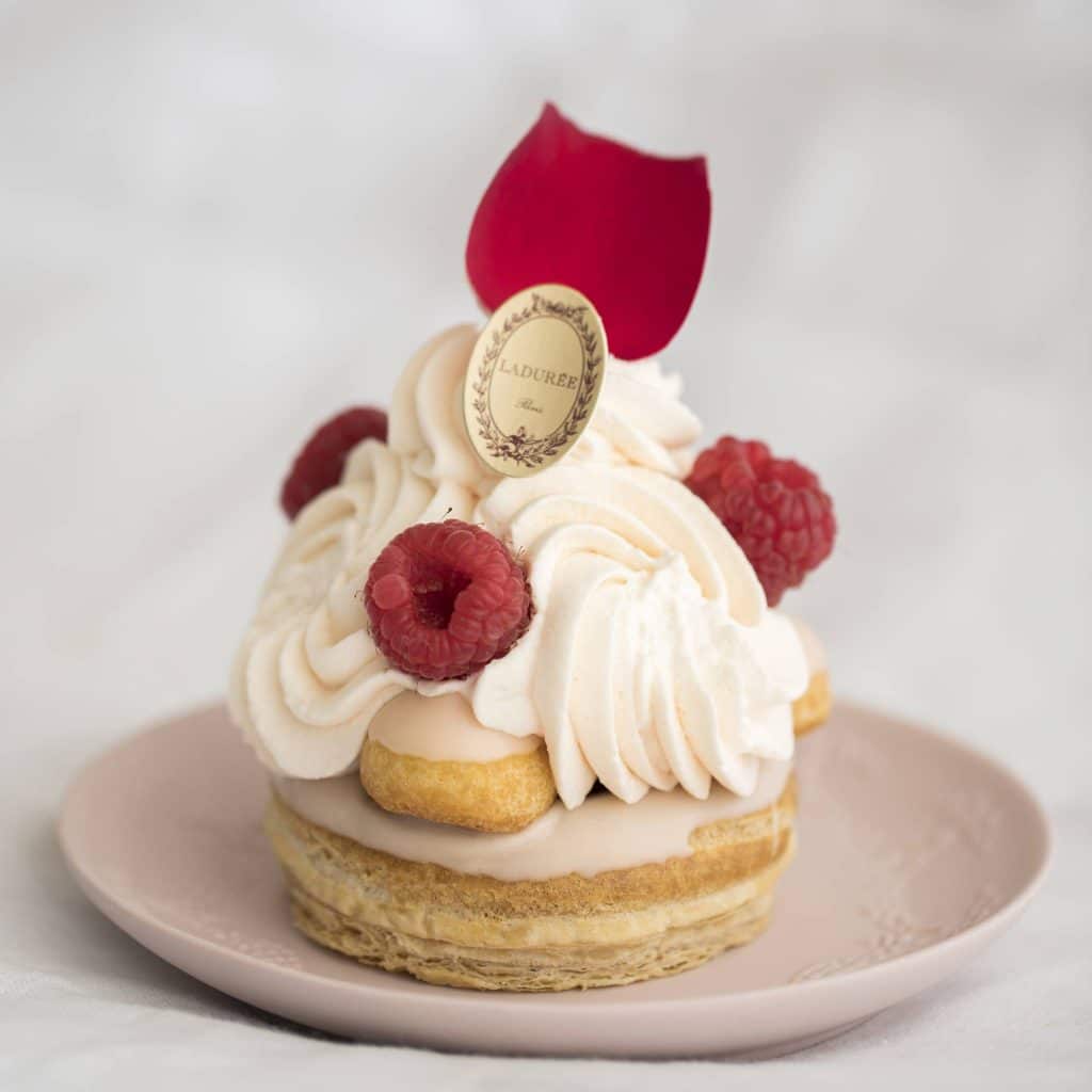 Succombez à la douceur de ce Saint-Honoré Rose Framboise garni d’une pâte feuilletée, d’une pâte à choux, d’une crème pâtissière allégée aux pétales de rose, de compote de framboise, d’un fondant au sirop de rose, le tout surmonté d’une crème Chantilly à l’eau de rose et de quelques framboises.