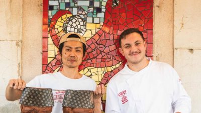 Daisuke Fukuda et un membre de l’équipe de La Carioca présentant leur panettone devant la mosaïque emblématique de la boulangerie à Sète