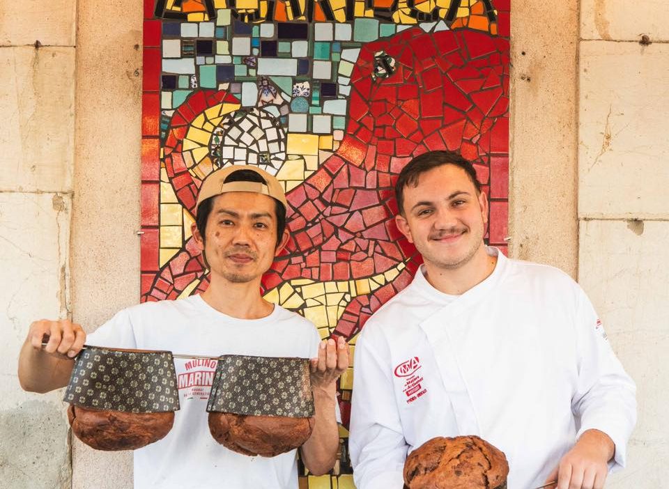 Daisuke Fukuda et un membre de l’équipe de La Carioca présentant leur panettone devant la mosaïque emblématique de la boulangerie à Sète
